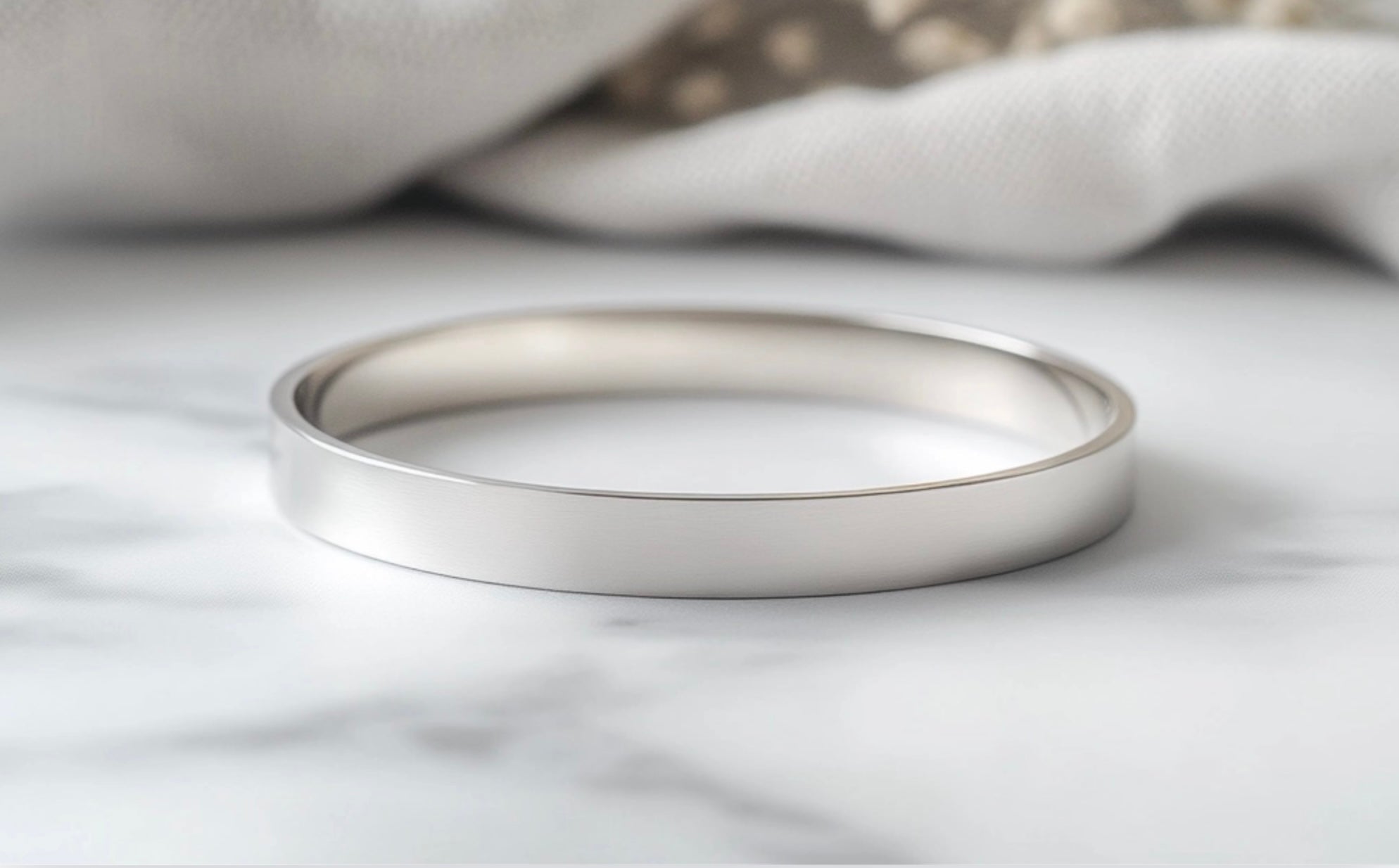 A sterling silver bangle on a pale grey polishing cloth, on a matt marble worktop