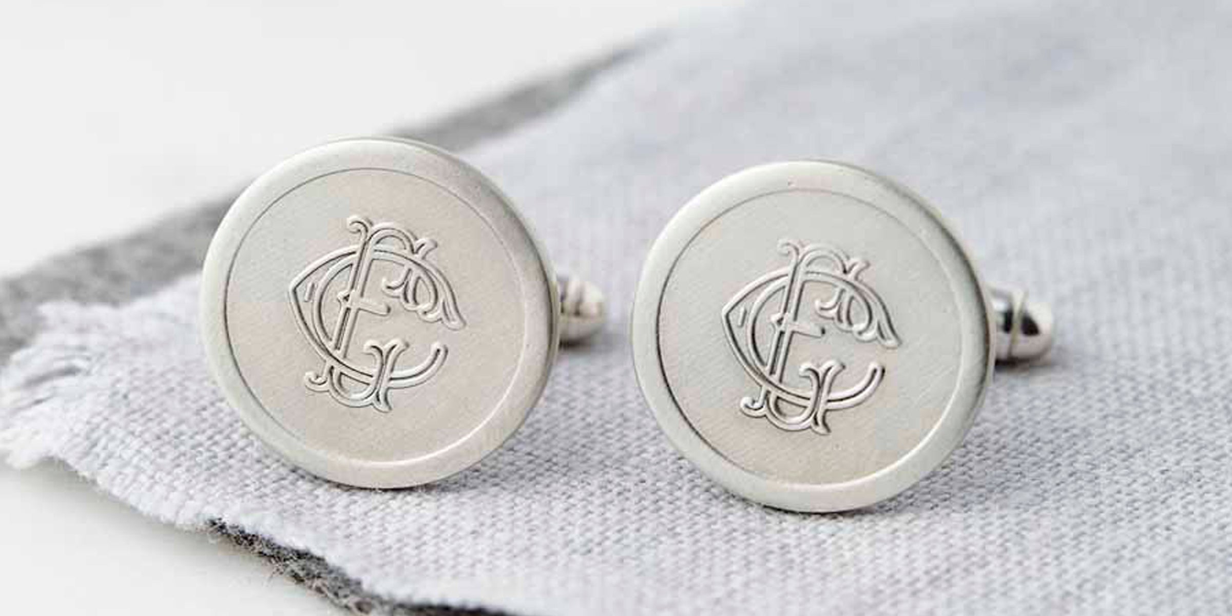Sterling silver cufflinks, engraved with a decorative monogram using the letters E and C on pale grey linen